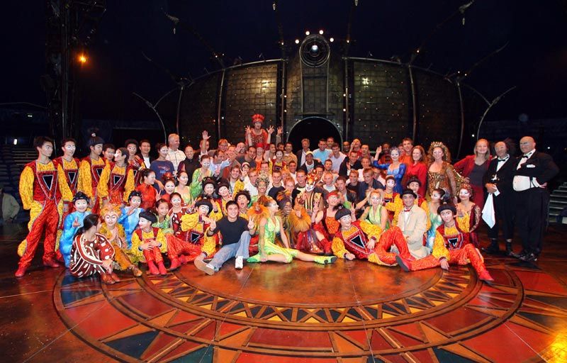 Eine große Gruppe von Menschen, einschließlich Darstellern in bunten Kostümen, posiert gemeinsam auf einer Bühne.