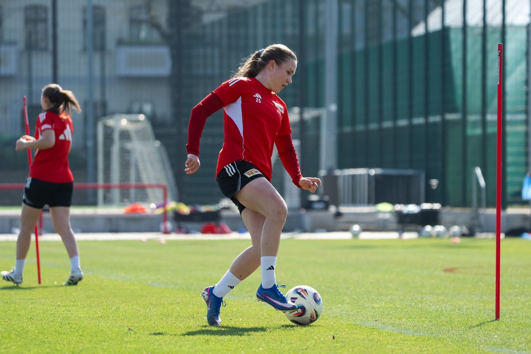 Eine Fußballspielerin in rotem Trikot dribbelt mit einem Ball auf einem Trainingsplatz.