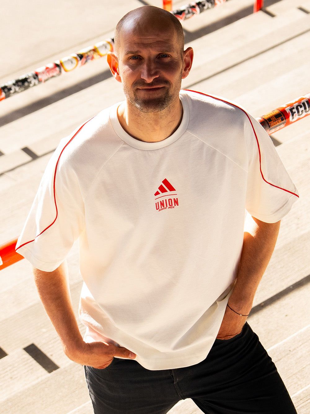 Mann steht auf einer Treppe und trägt ein weißes T-Shirt mit roten Akzenten und dem Adidas-Logo.