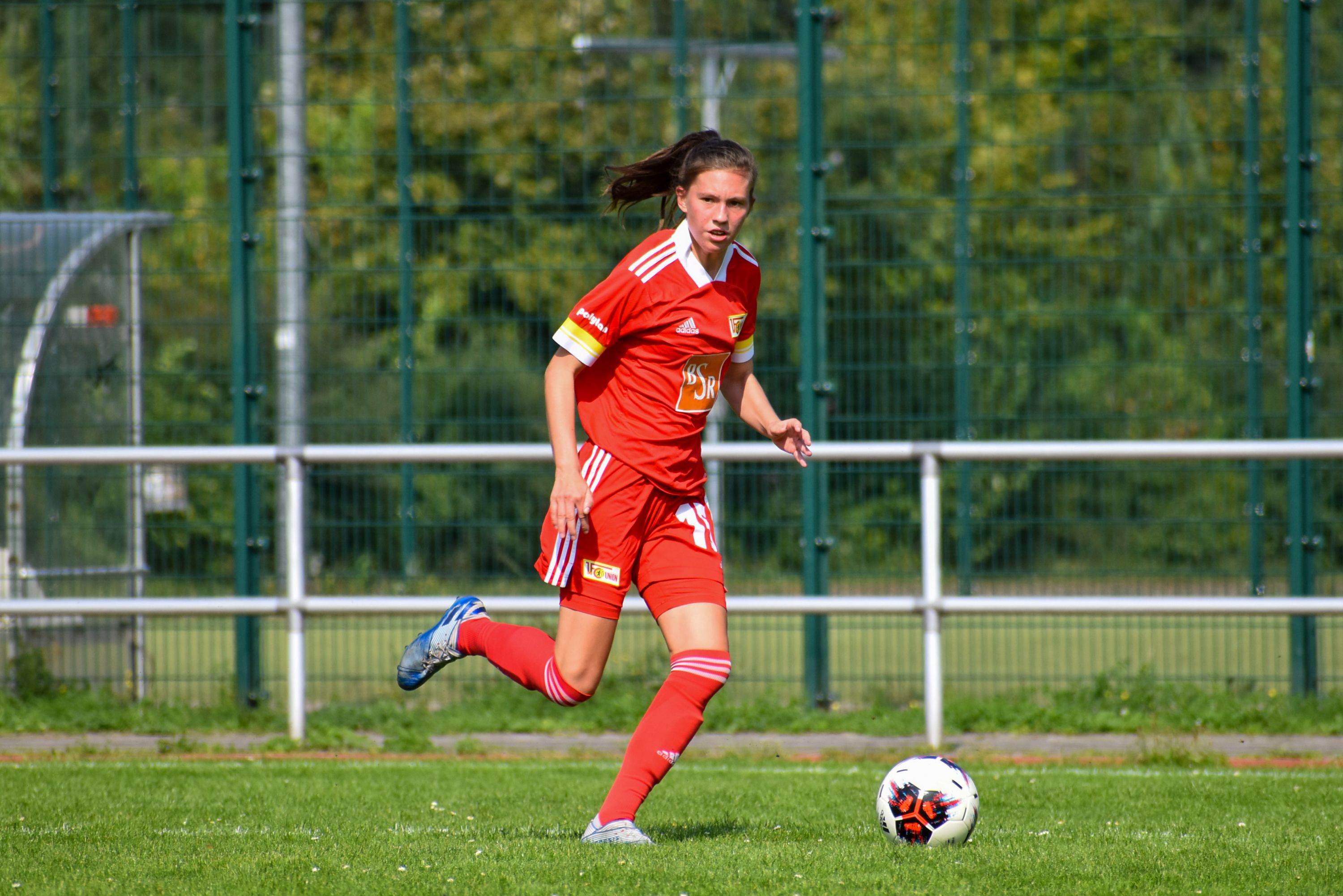 Eine Frau in einem roten Trikot läuft mit einem Fußball. Sie ist auf dem Spielfeld.