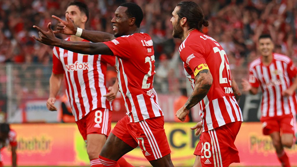Players celebrate a goal in red-and-white jerseys, surrounded by cheering fans in the stadium.