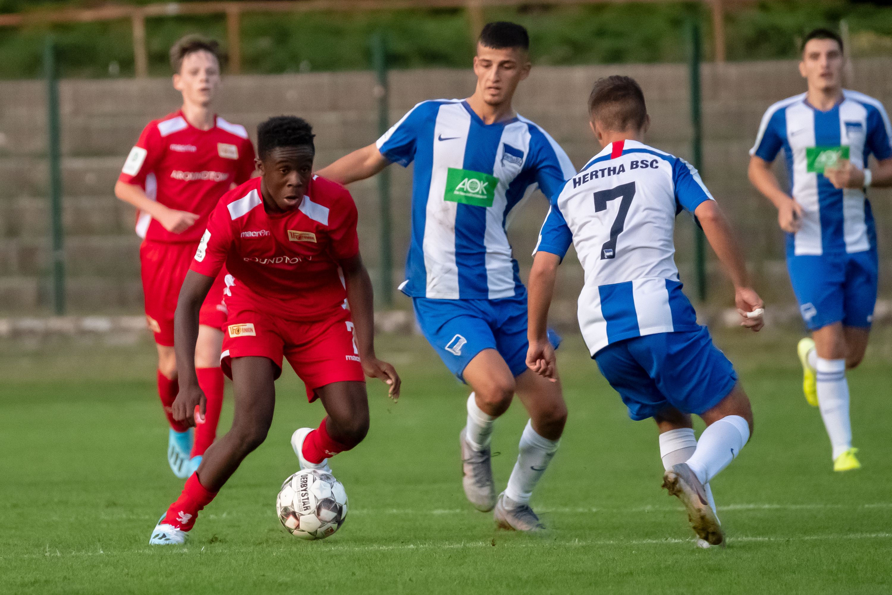 Zwei Gruppen von jungen Fußballspielern auf dem Spielfeld, während ein Spieler den Ball kontrolliert.