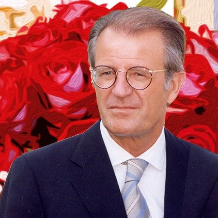 Ein Mann in Anzug mit Brille vor einem Hintergrund aus roten Rosen.