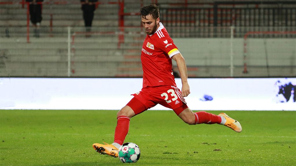A soccer player in a red uniform kicks the ball on a stadium field.