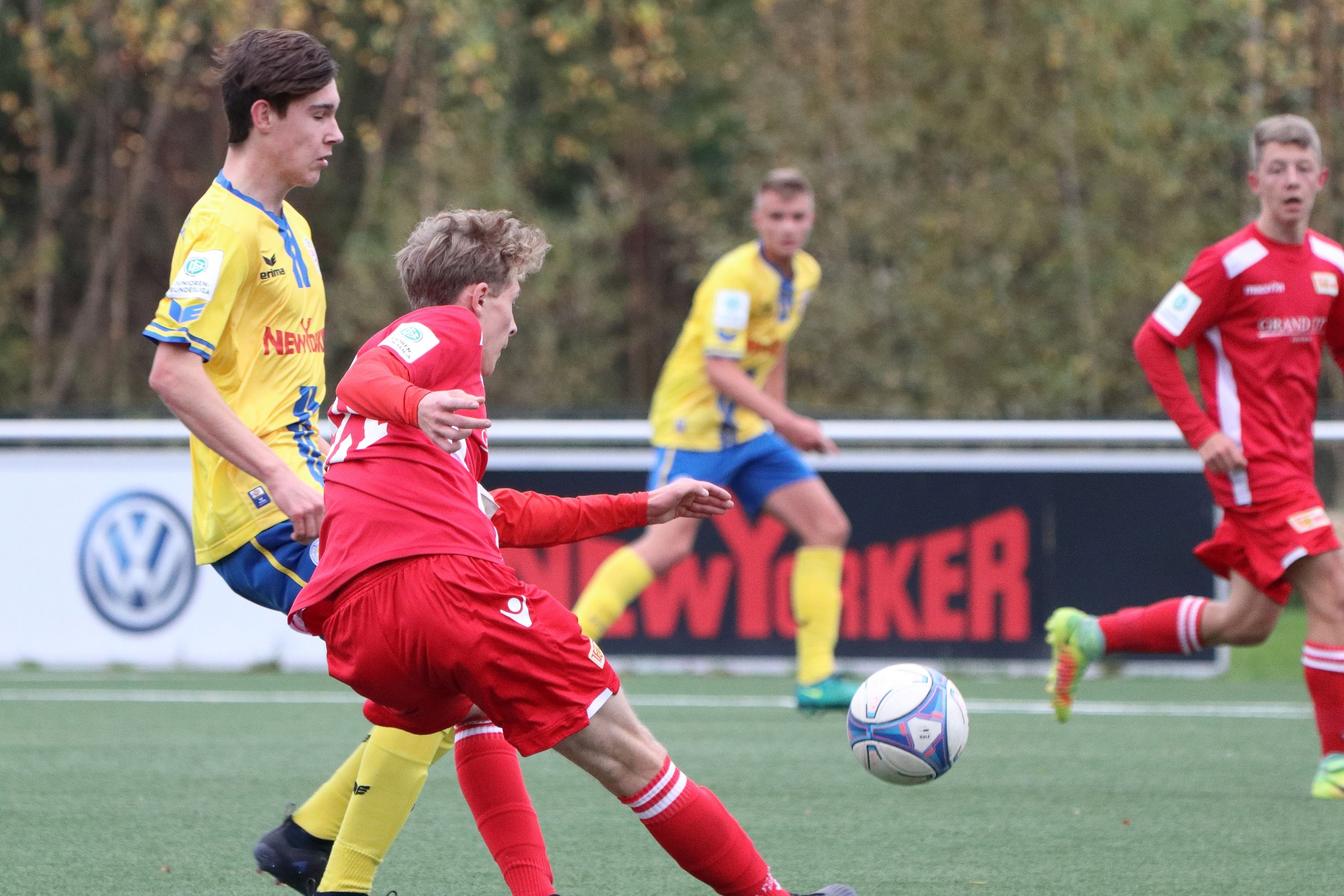 Zwei junge Fußballspieler stehen auf dem Platz. Einer trägt ein rotes Trikot. Der andere trägt ein gelbes Trikot. Sie spielen gerade mit einem Ball.