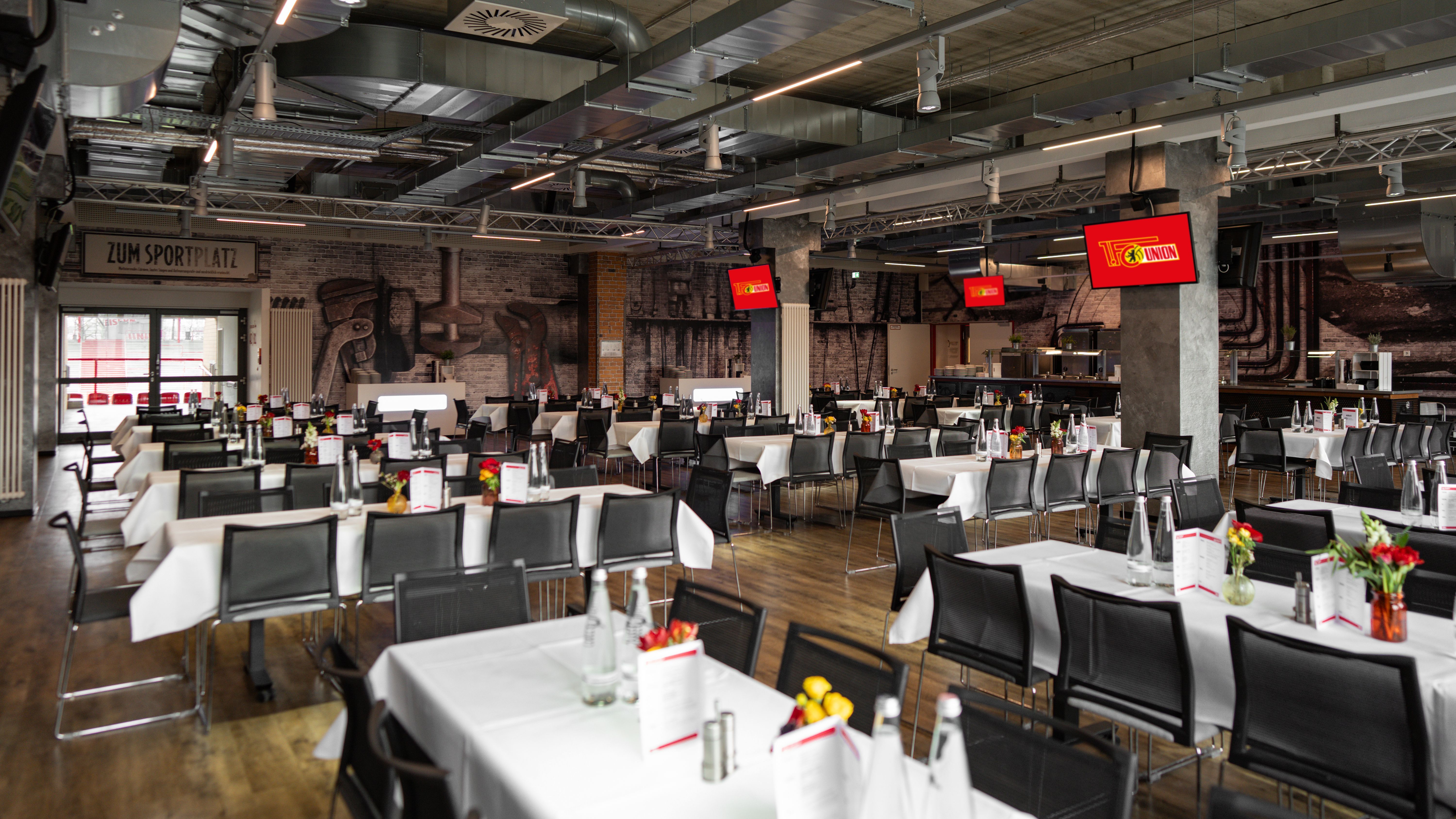 A modern restaurant with several tables, decorated with flowers, drinks, and menus, in a stylish industrial ambiance.