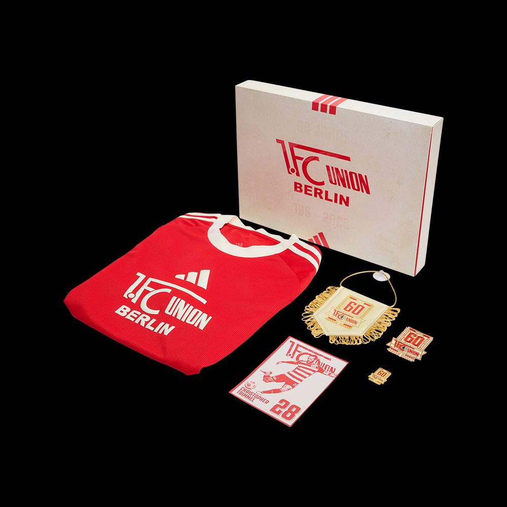 Ein rotes Fußballtrikot mit "1. FC Union Berlin" Logo, umgeben von Medaillen und einer Geschenkbox.