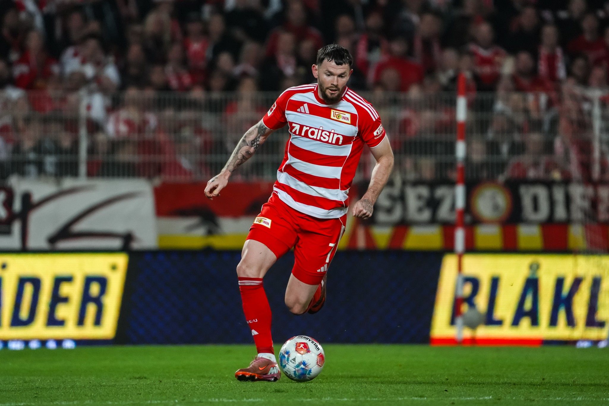 Ein Fußballspieler in rot-weißem Trikot führt den Ball auf dem Spielfeld während eines Spiels.