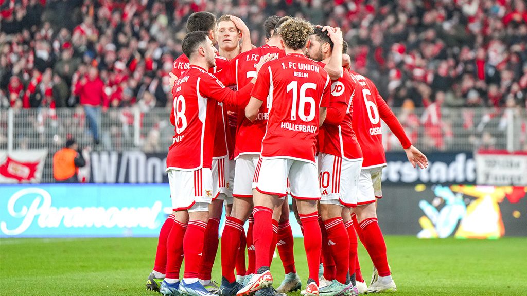Players of 1. FC Union Berlin in red jerseys celebrate a goal amidst cheering fans in the stadium.