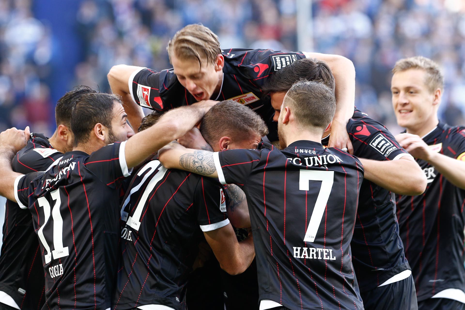 Fußballspieler freuen sich nach einem Tor. Viele Fans sind im Hintergrund.