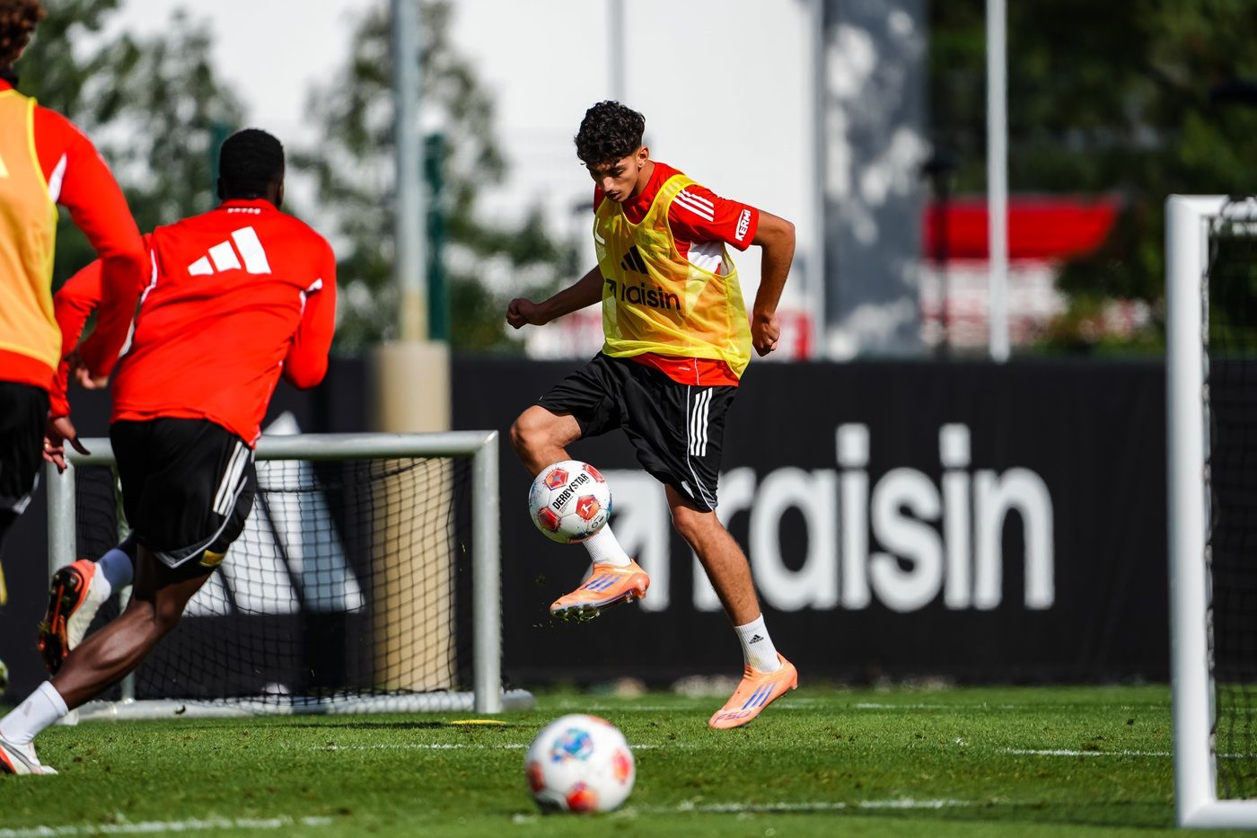 Ein Fußballspieler dribbelt den Ball während des Trainings, umgeben von anderen Spielern in roten Trikots.