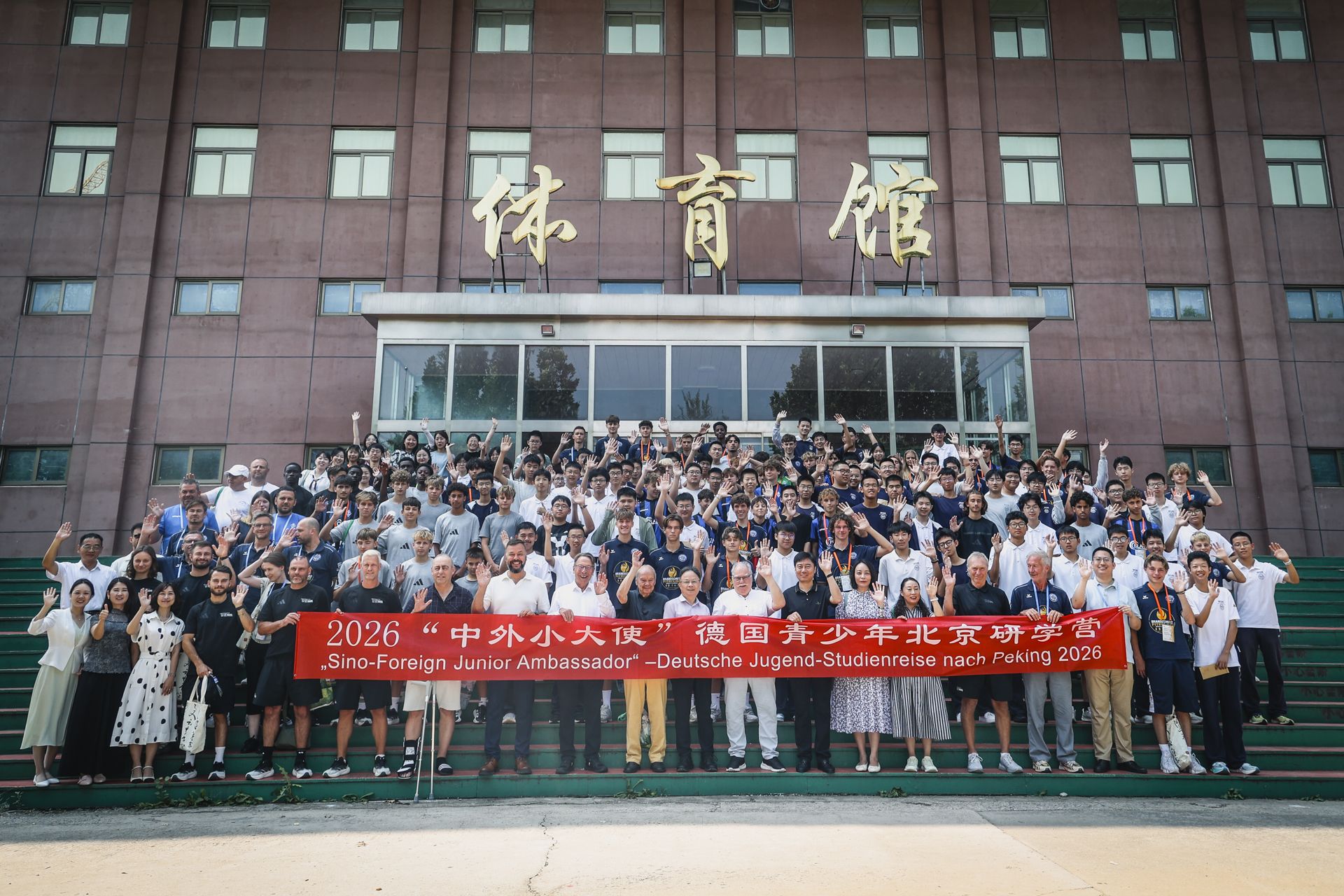 Gruppenfoto von Teilnehmern eines Jugendprogramms in Peking, vor einem Gebäude, mit Banner und lächelnden Gesichtern.