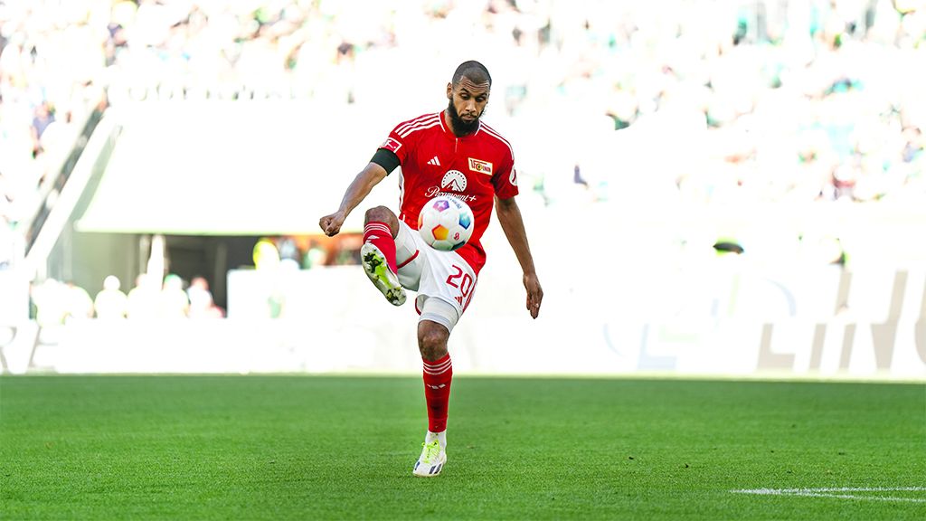 A soccer player in a red jersey controls the ball on a green field.