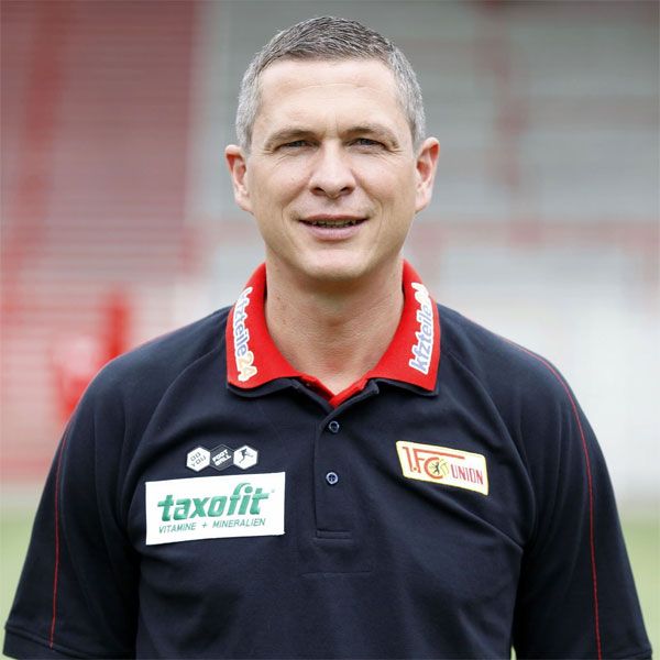 Porträt eines Mannes in einem schwarzen Poloshirt mit rotem Kragen und dem Logo von 1. FC Union Berlin.