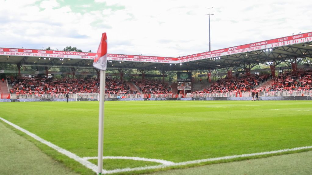 Ein Blick auf das Fußballfeld in einem Stadion, mit einer Eckfahne und Zuschauern auf den Tribünen.
