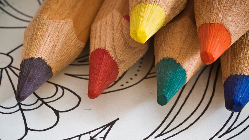 Sechs Buntstifte in verschiedenen Farben liegen auf einem unvollendeten Ausmalbild mit floralen Motiven.