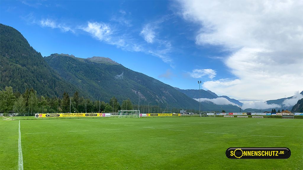 Panoramic view of a football field with mountains and cloudy sky in the background.