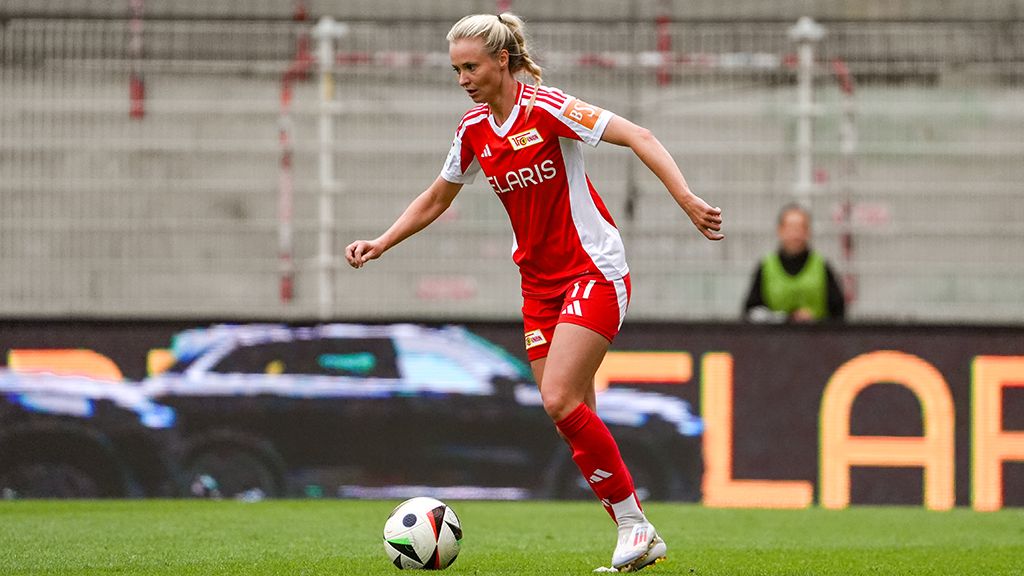 A female soccer player in a red jersey dribbles the ball on the field.