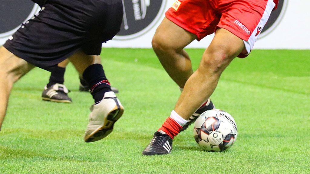 Ein naher Blick auf die Beine von zwei Fußballspielern, die um einen Ball auf einem grünen Spielfeld kämpfen.