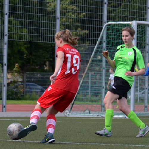 Eine Fußballspielerin in rotem Trikot schießt den Ball, während eine gegnerische Spielerin in grün zuschaut.