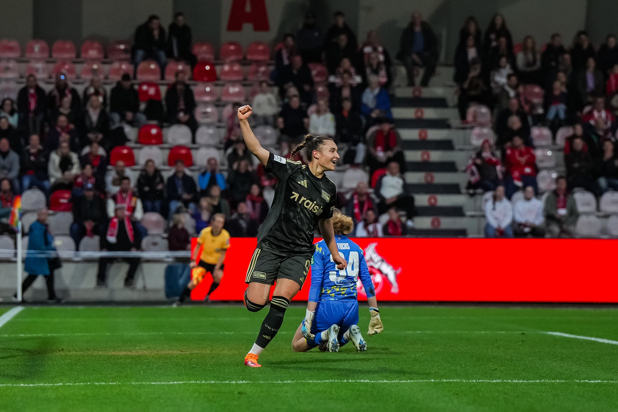 Eine Spielerin jubelt nach einem Tor, während der Torwart am Boden sitzt. Leere Stadionplätze im Hintergrund.