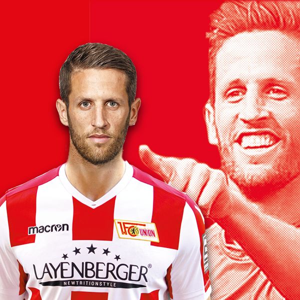 Ein Fußballspieler in einem rot-weiß gestreiften Trikot mit lächelndem Gesichtsausdruck vor einem roten Hintergrund.