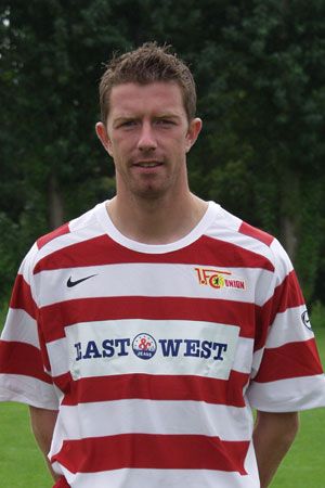 Ein Mann in gestreiftem Fußballtrikot steht vor unscharfem Hintergrund auf einem grünen Platz.