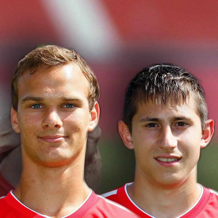 Zwei junge Männer in roten Trikots mit neutralem Ausdruck stehen nebeneinander vor einem verschwommenen Hintergrund.