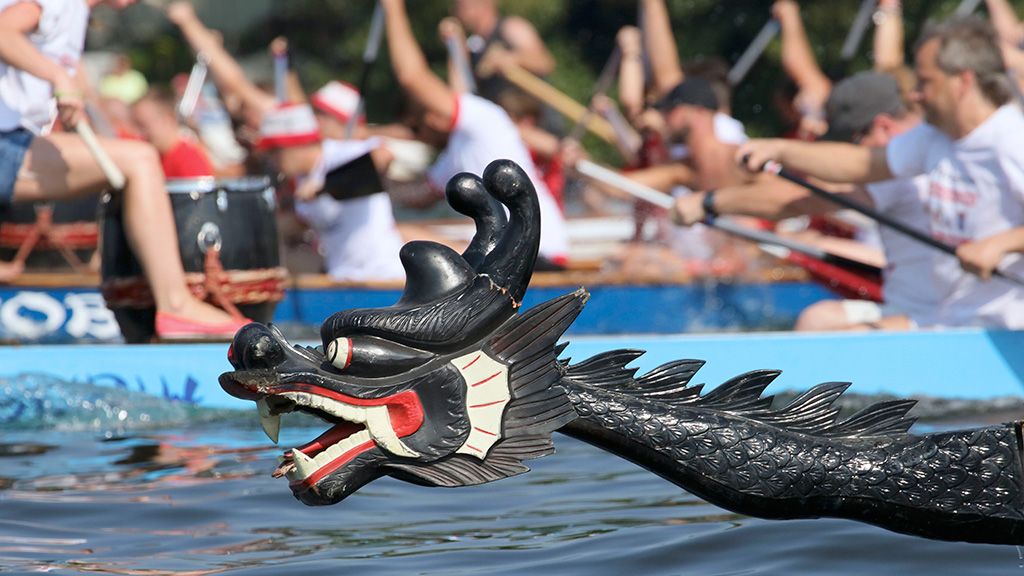 A black dragon head emerges from the water, while a dragon boat with paddling participants is visible in the background.