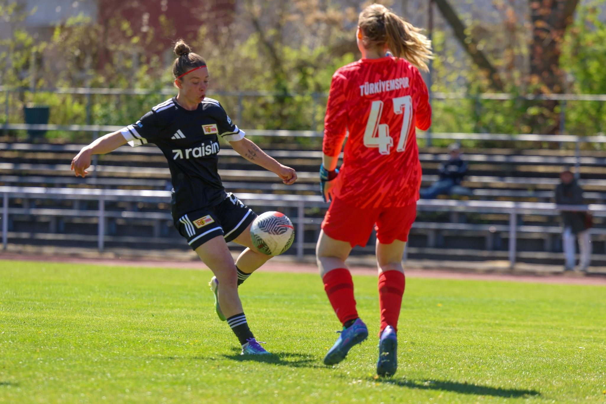 Eine Fußballspielerin dribbelt den Ball, während die Torhüterin in gestreifter Kleidung bereit steht.