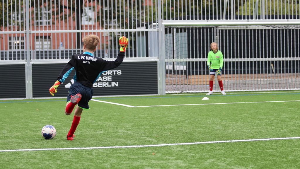 Ein junger Torwart in schwarzem Trikot springt, um einen Ball abzufangen, während ein weiterer Spieler im Hintergrund steht.