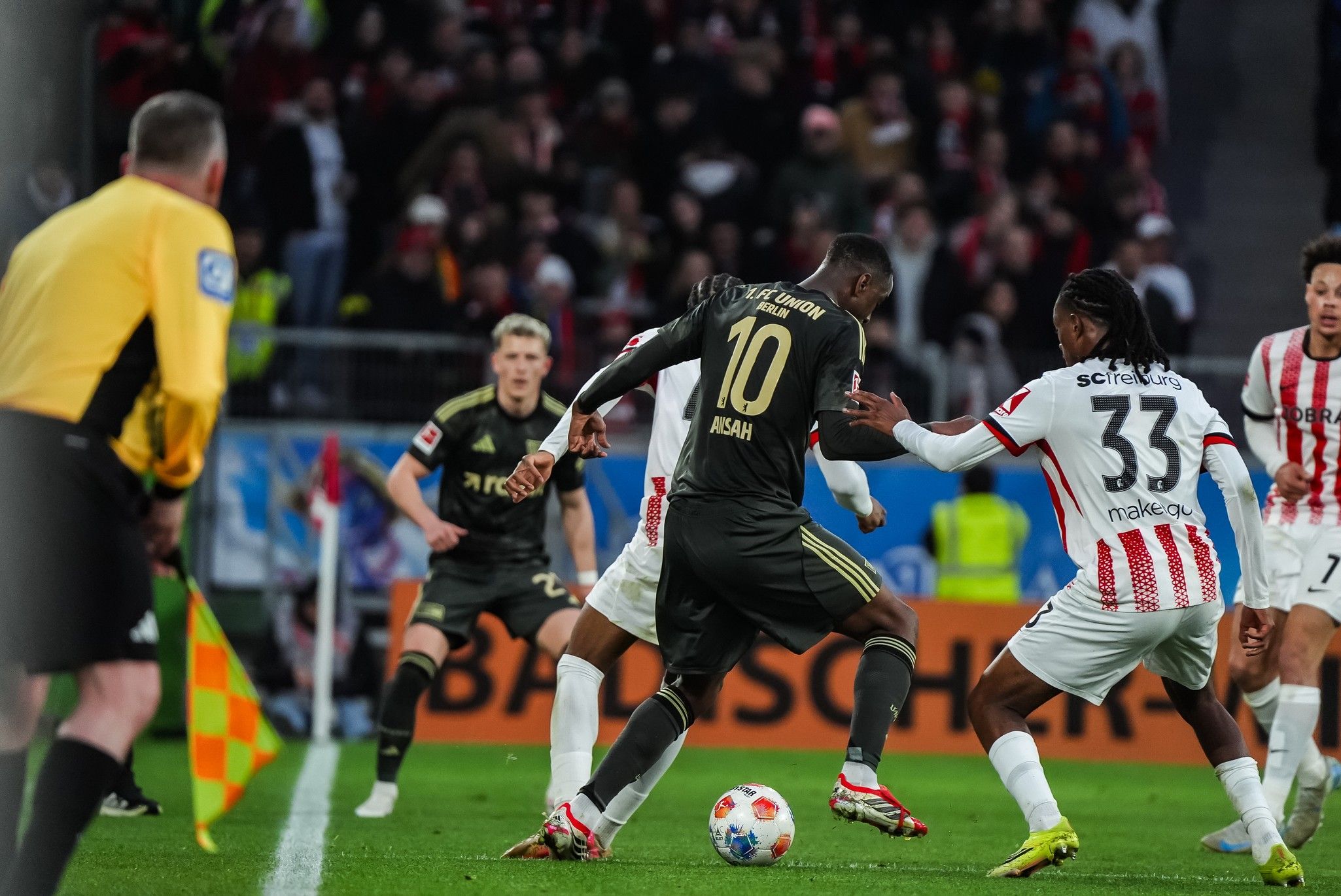 Ein Fußballspieler mit der Nummer 10 dribbelt den Ball, während zwei Gegenspieler ihn zu stoppen versuchen.