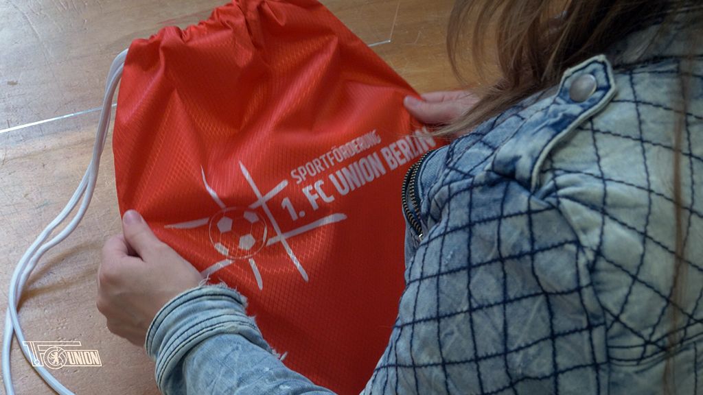 Eine Person hält einen roten Rucksack mit dem Logo des 1. FC Union Berlin in den Händen.