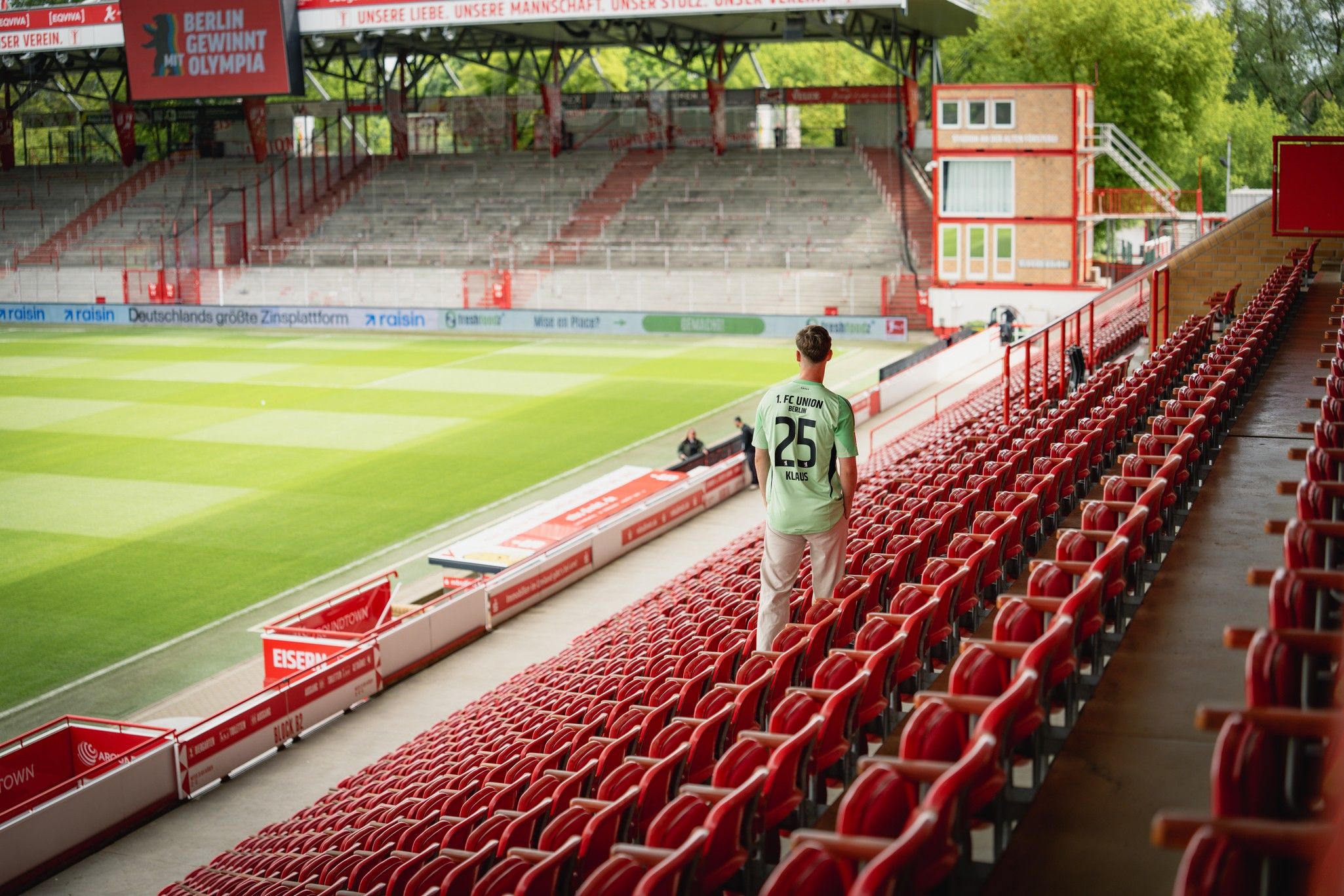 Ein Mensch in einem Trikot mit der Nummer 25 steht auf den roten Sitzplätzen eines Fußballstadions.