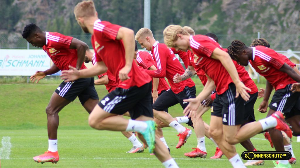 Spieler trainieren auf einem grünen Fußballfeld, während sie in einem Sprintlauf aktiv sind.