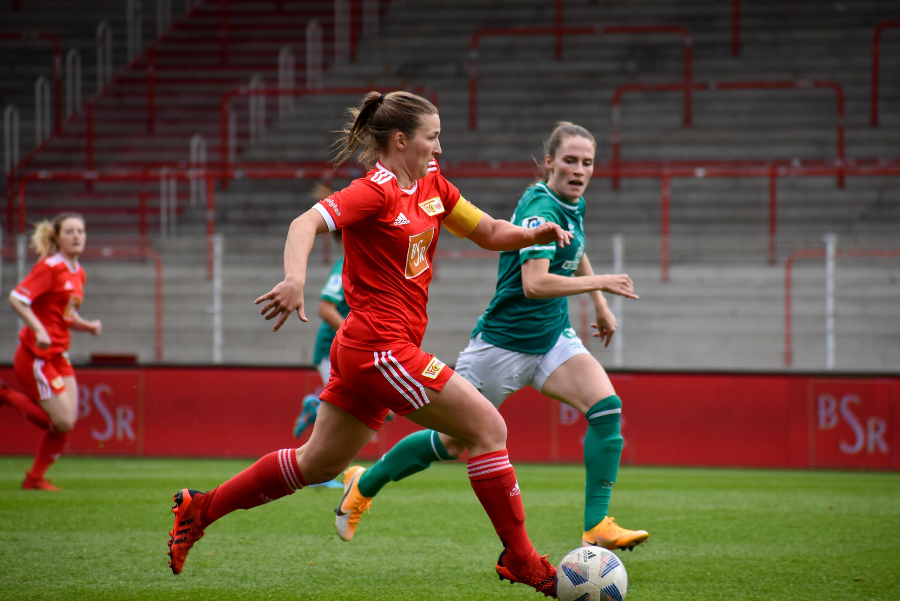 Zwei Frauenfußballspielerinnen in Aktion, eine im roten Trikot mit der Nummer 8 und die andere in grün, auf einem Rasenplatz.