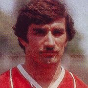 Porträt eines Mannes mit kurzem, dunklem Haar und Schnurrbart, trägt ein rotes Sporttrikot.