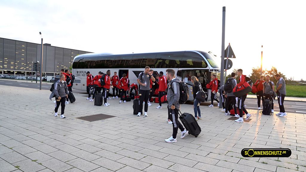 A group of people in sportswear is standing in front of a tour bus while organizing their luggage.