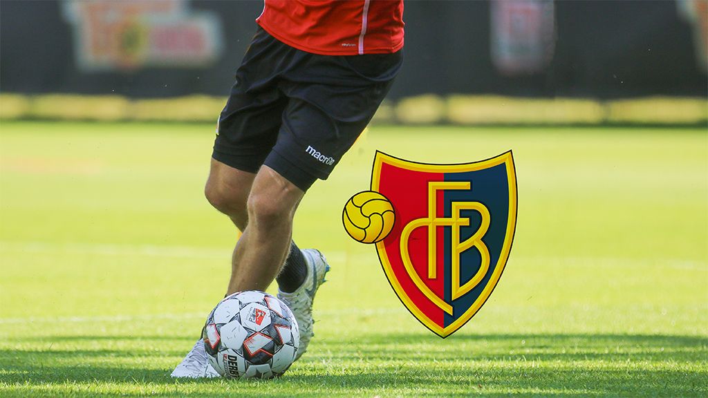 Ein Spieler dribbelt einen Fußball auf einem Rasenplatz, daneben das Logo des FC Basel.