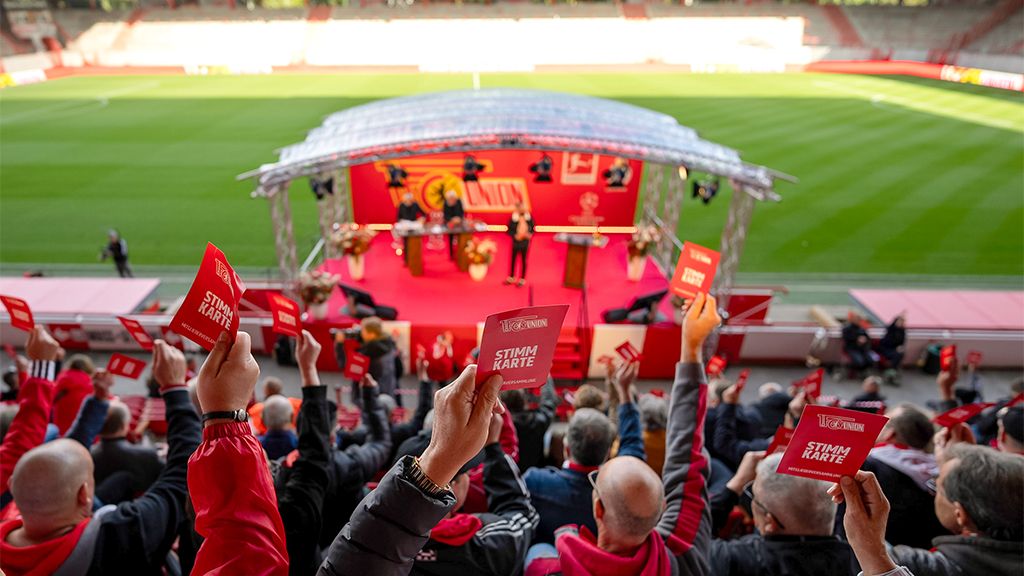 Fans halten rote Karten in einem Stadion hoch, während eine Veranstaltung auf der Bühne stattfindet.