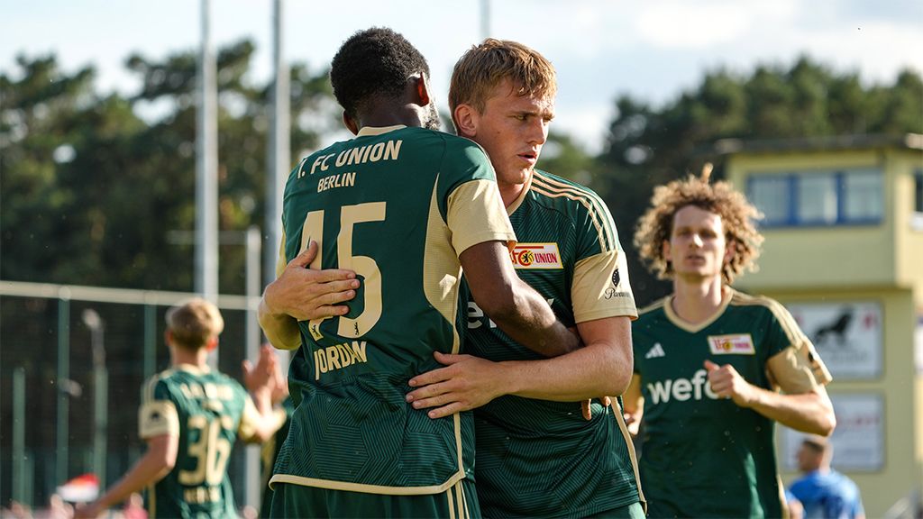 Zwei Fußballspieler des 1. FC Union Berlin umarmen sich nach einem gelungenen Spielzug, im Hintergrund sind weitere Spieler sichtbar.