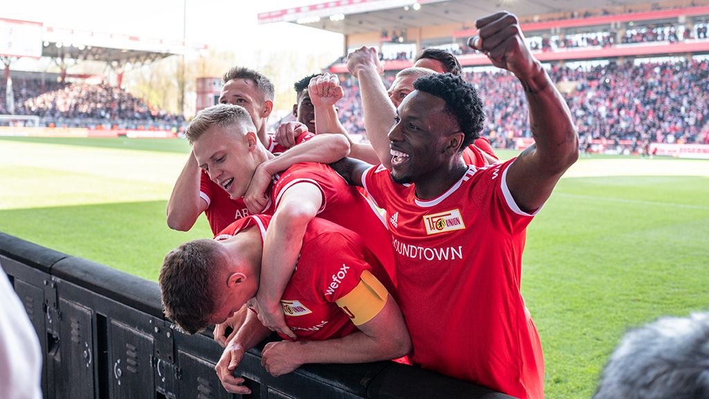Fußballspieler in roten Trikots feiern. Die Fans im Stadion jubeln.