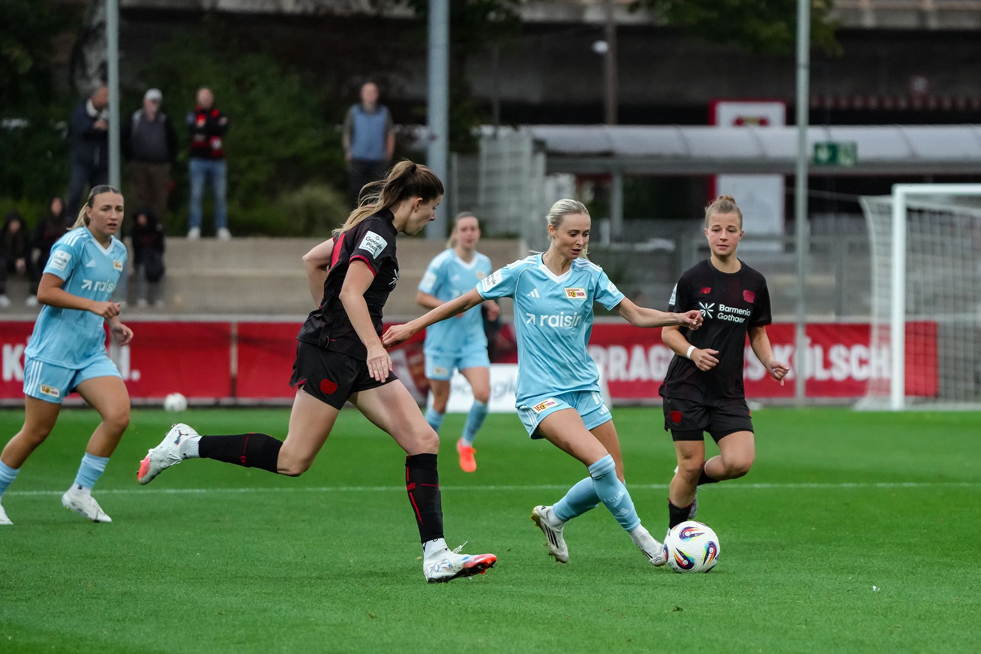 Zwei Fußballspielerinnen im Wettlauf um den Ball während eines Spiels auf einem grünen Rasenplatz.