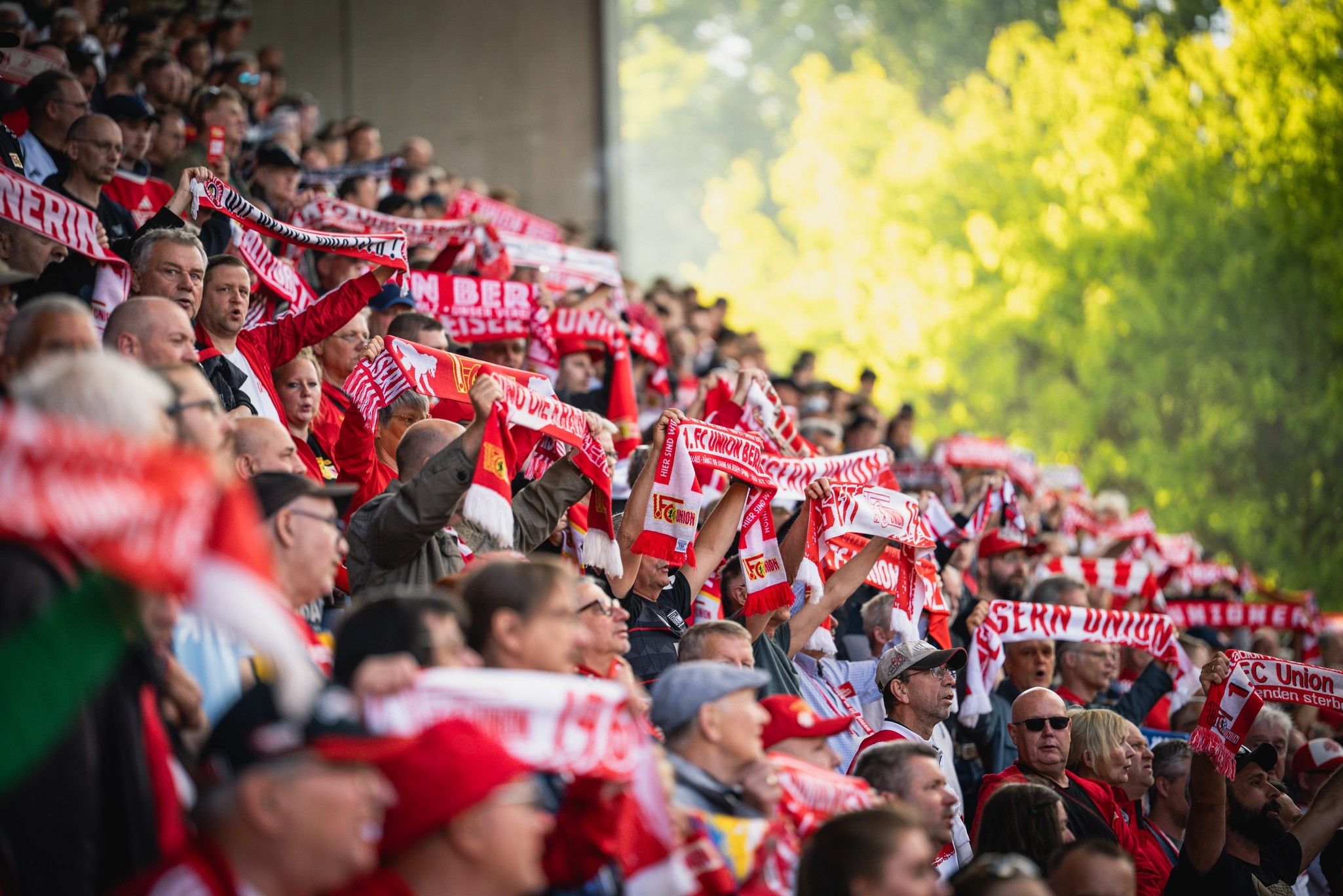 Eine Menschenmenge im Stadion hält rote Schals mit dem Schriftzug "Union" und feuert ihre Mannschaft an.