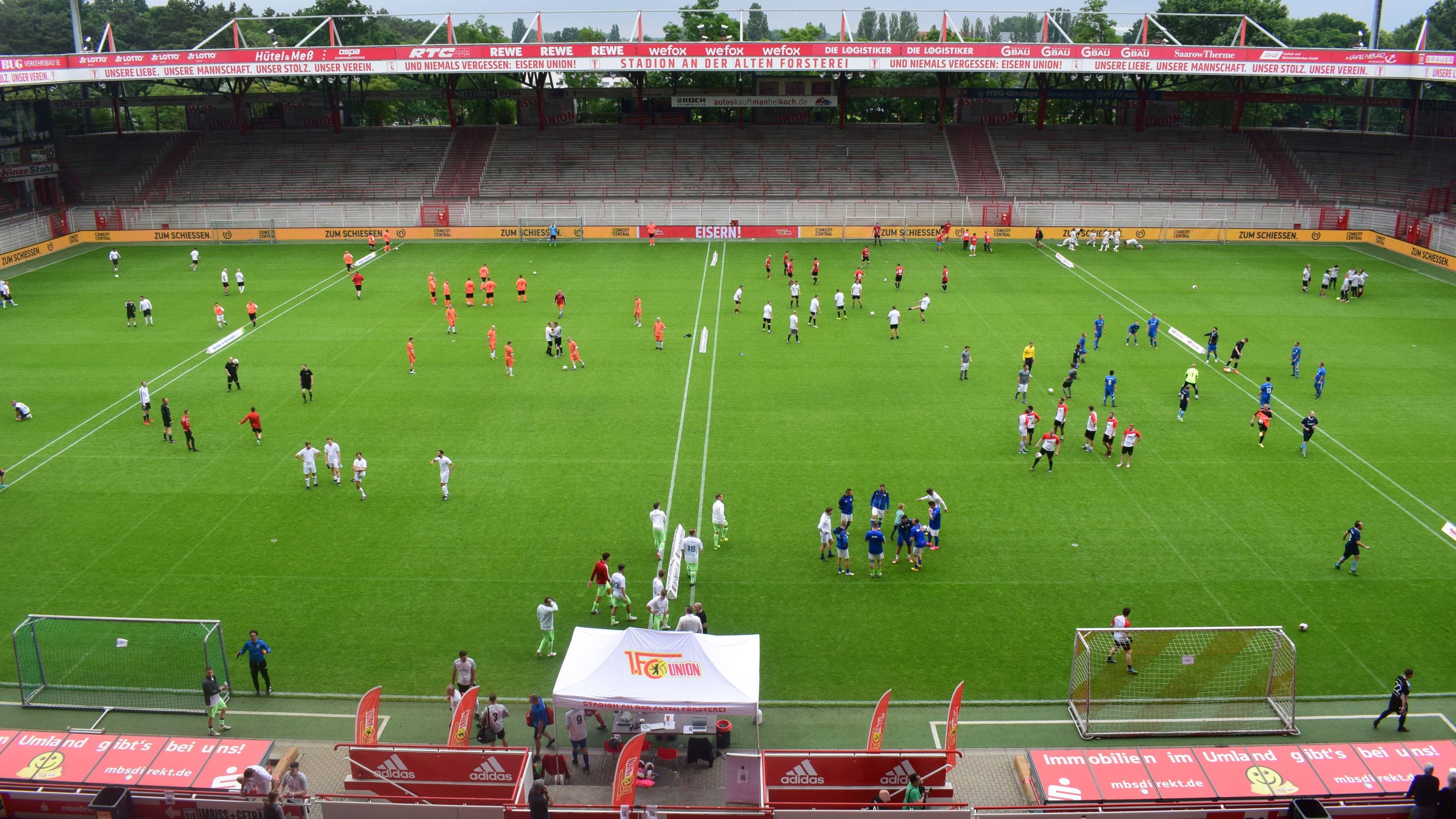 Eine Sportveranstaltung in einem Stadion, mit Spielern in verschiedenen Trikots, die auf dem Rasen trainieren und spielen.