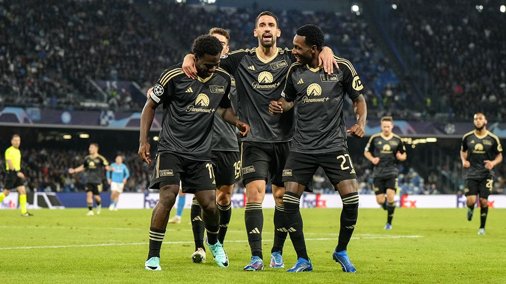 Vier Fußballspieler in schwarzen T-Shirts freuen sich über ein Tor.