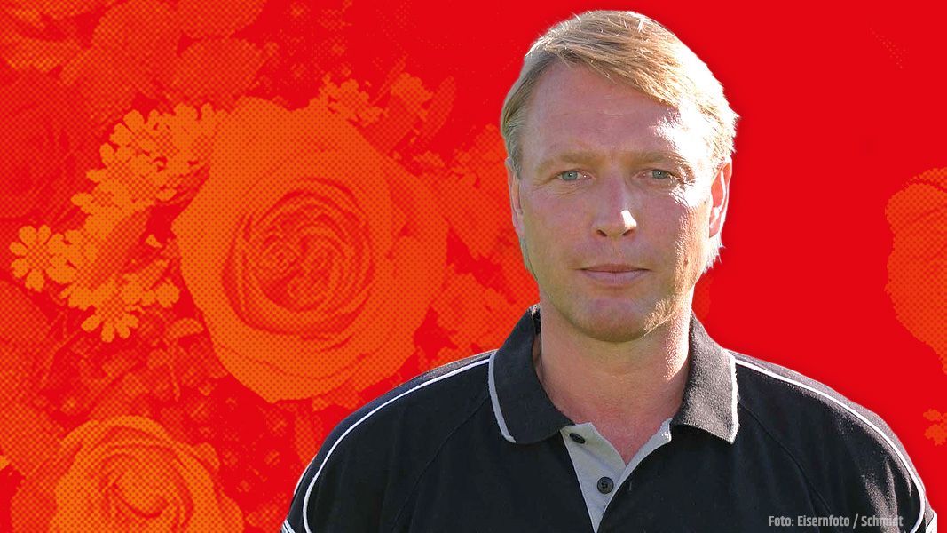 Porträt eines Mannes mit blonden Haaren vor einem roten Hintergrund mit Blumenmotiven. Er trägt ein schwarzes Poloshirt.