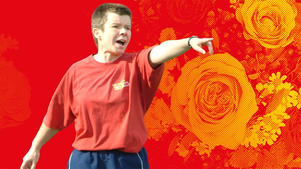 Eine Person in rotem T-Shirt zeigt gestenreich und wirkt engagiert, vor einem bunten, floral-musternden Hintergrund.