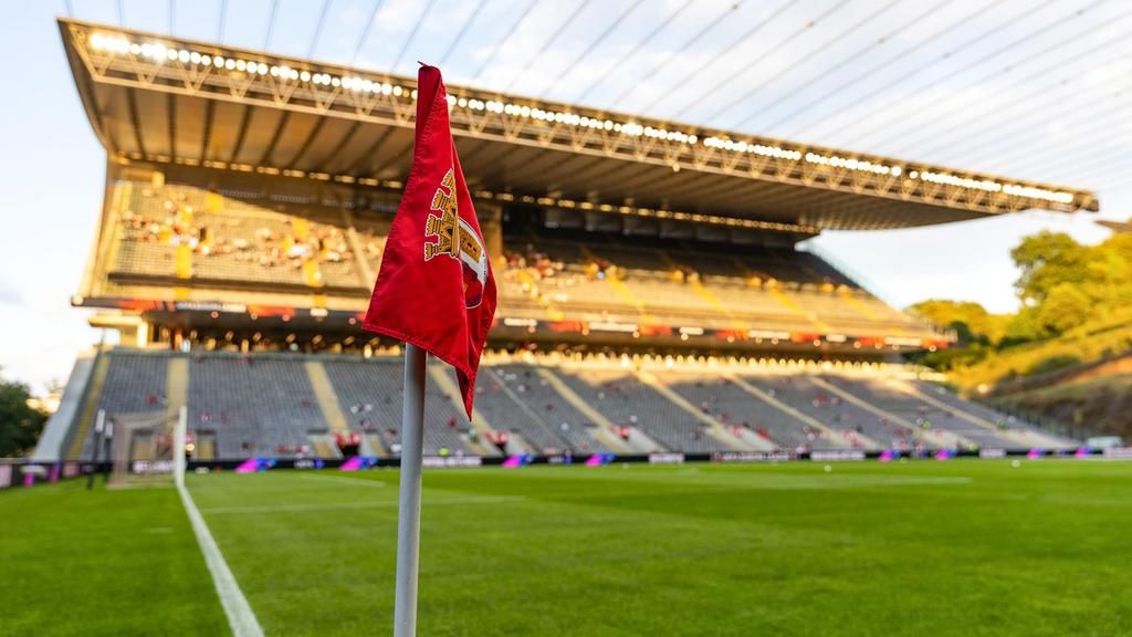 Eckfahne in einem Fußballstadion mit leeren Tribünen und Sonnenlicht auf dem Spielfeld.