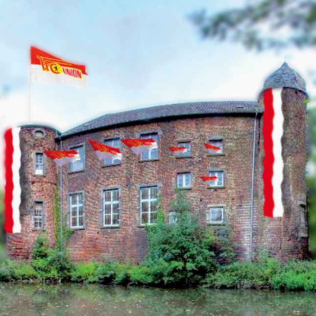 Historisches Gebäude mit roten und weißen Flaggen, umgeben von Wasser und Bäumen.